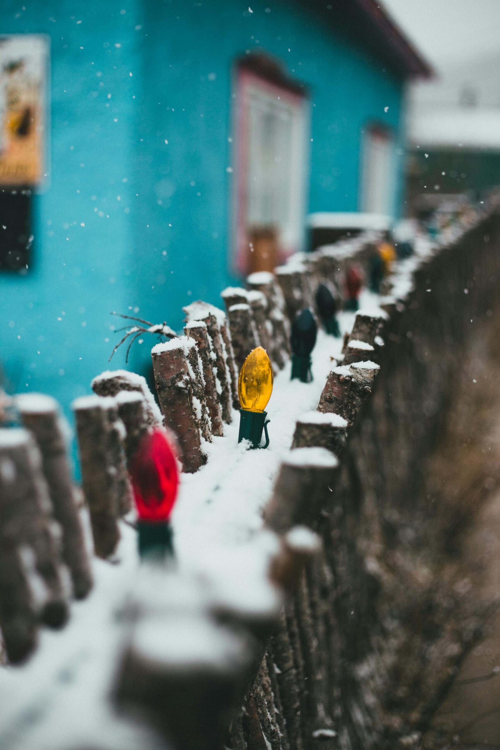Bright multicolored garland hanging on wooden fence of rural house in village under snowfall